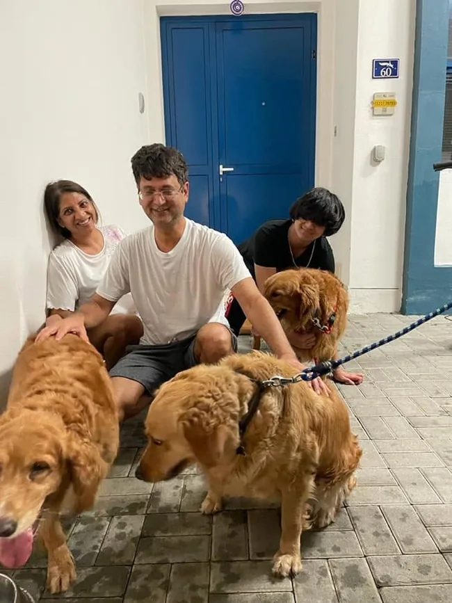 A family outside their home with their three golden dogs.