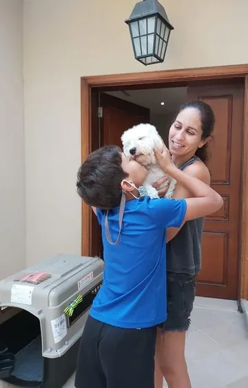 A mother and child embracing their white dog at home beside a travel crate.