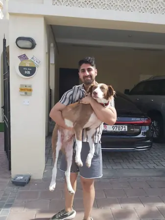 A man holding his dog outside his home.