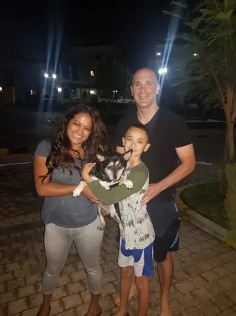 A family holding their small dog outdoors in the evening.